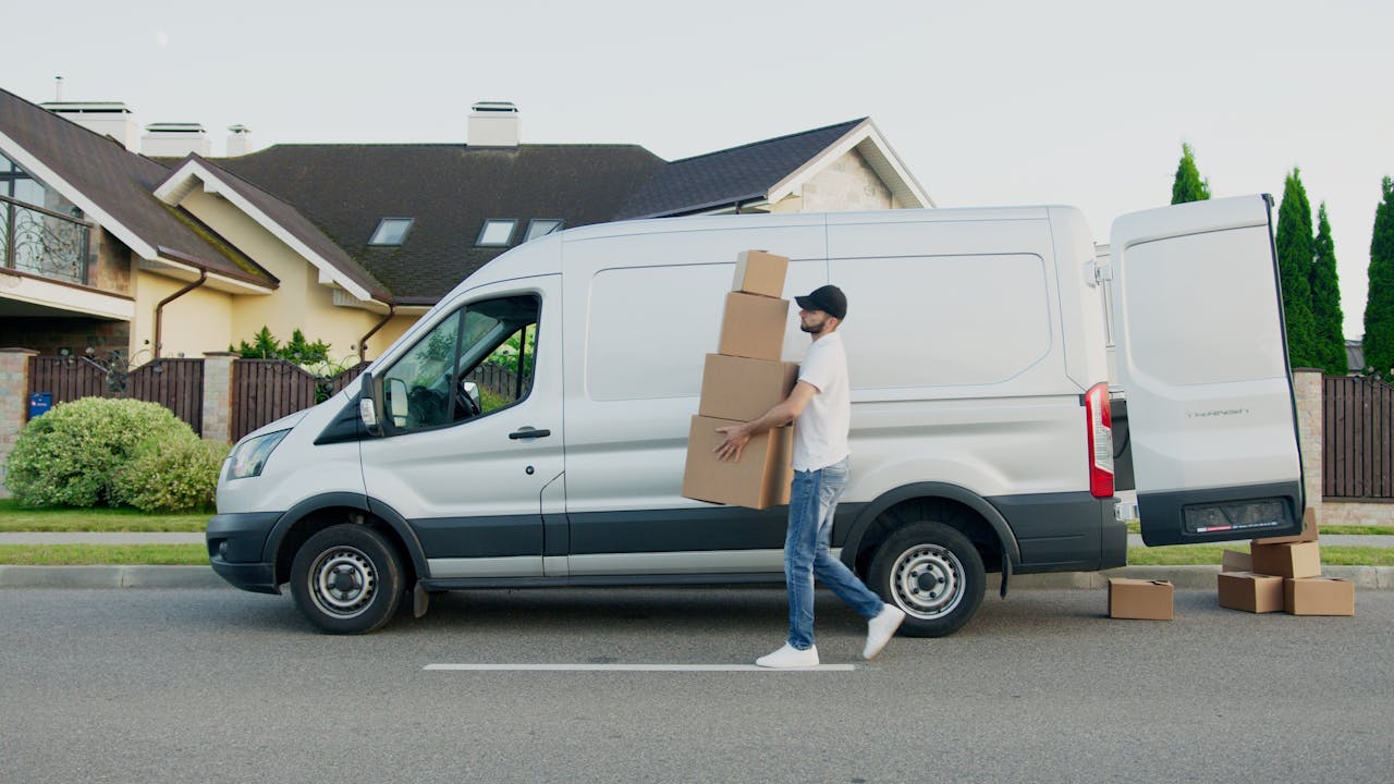 home-hero Man unloading cardboard boxes from a delivery van in a suburban neighborhood street.